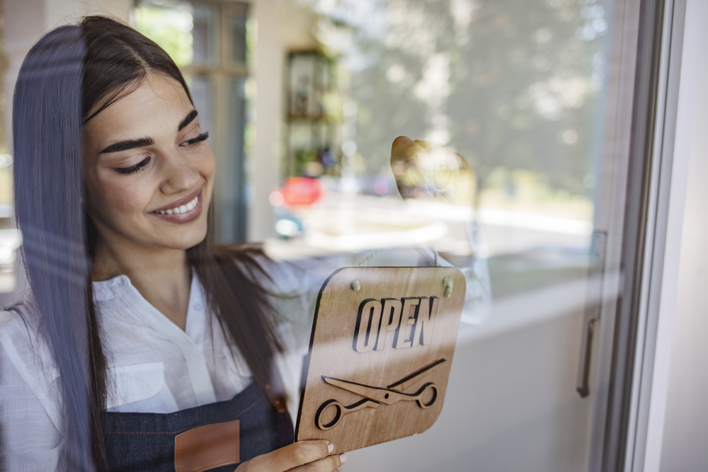 Young businesswoman turning open sign in store window